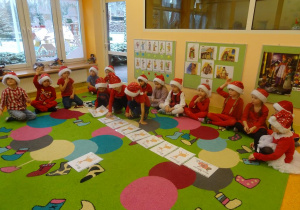 Grupa dzieci siedzi wokół ilustracji rozłożonych na dywanie, troje dzieci przekłada ilustrację.